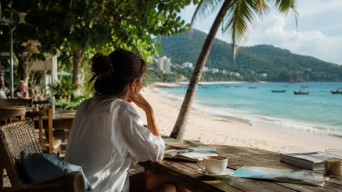 Traveler thoughtfully researching relaxed Phuket holiday experiences from a beachfront café in Thailand