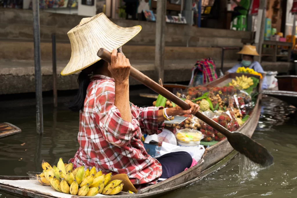 Must see attractions Thailand featuring a traditional vendor at Damnoen Saduak Floating Market near Bangkok.