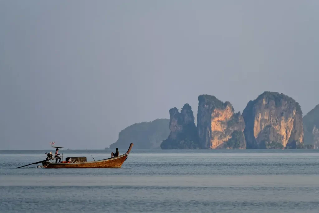 Longtail boat cruising past Krabi's iconic limestone cliffs, showcasing one of the most spectacular destinations for travellers deciding where to go in Southern Thailand.