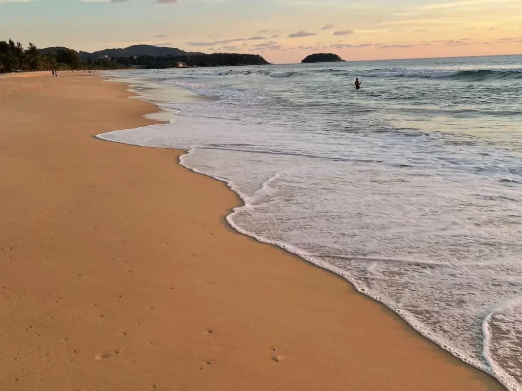 Karon Beach in Phuket, one of the best places to visit when deciding where to go in Southern Thailand, featuring golden sand, gentle waves and a tropical coastline.