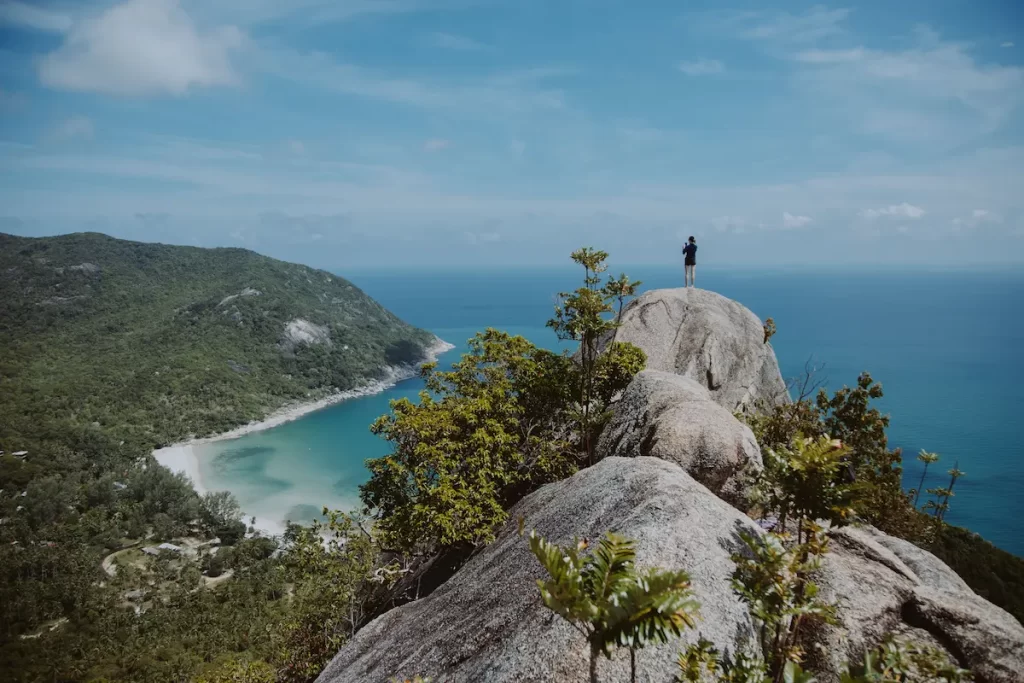 Why visit Thailand? Hiker enjoying spectacular coastal views from a rocky viewpoint overlooking a tropical bay.