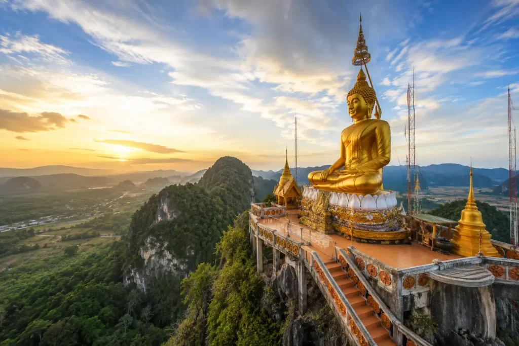 Golden Buddha at Tiger Cave Temple in Krabi, one of the must-see attractions in Southern Thailand, overlooking limestone mountains and rainforest.
