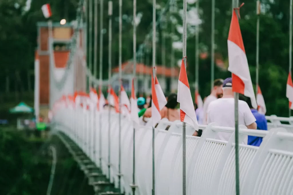 Indonesian flags lining a suspension bridge with travellers walking through Indonesia, representing the country's culture, identity and diverse travel experiences.
