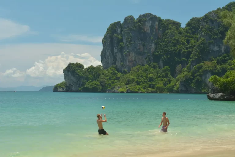 People enjoying a tropical beach surrounded by limestone cliffs in Thailand, shoing just one of the reasons people visit Thailand