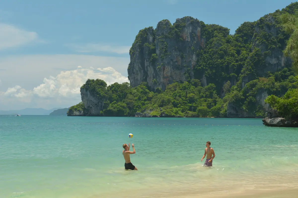 People enjoying a tropical beach surrounded by limestone cliffs in Thailand, shoing just one of the reasons people visit Thailand