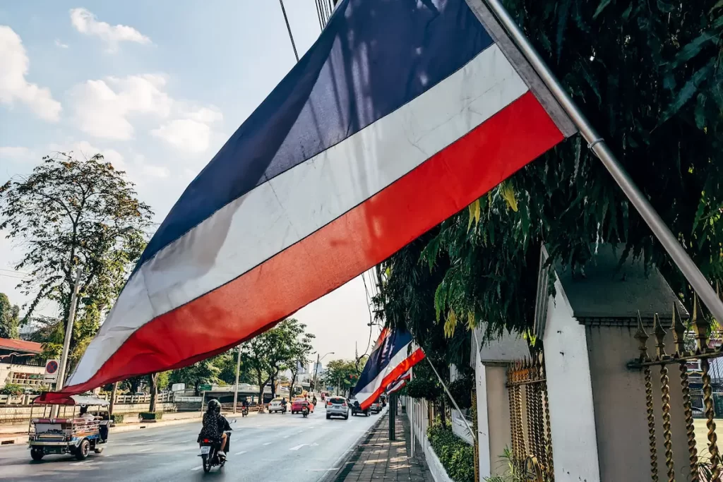Thai flags lining a city street with a tuk tuk travelling through Thailand, representing the country's culture, identity and everyday travel experience.