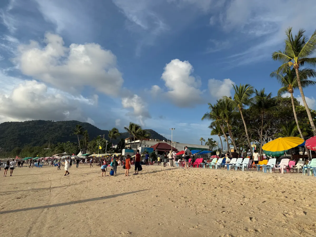 Visitors enjoying the busy central section of Patong Beach with beach chairs, umbrellas and palm trees featured in our Patong Travel Guide.
