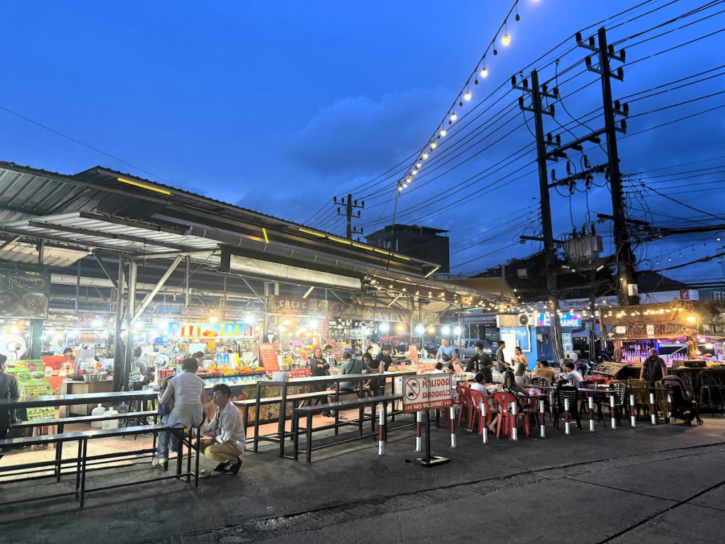 Exterior evening view of Malin Plaza Patong with market stalls, seating and surrounding street activity.