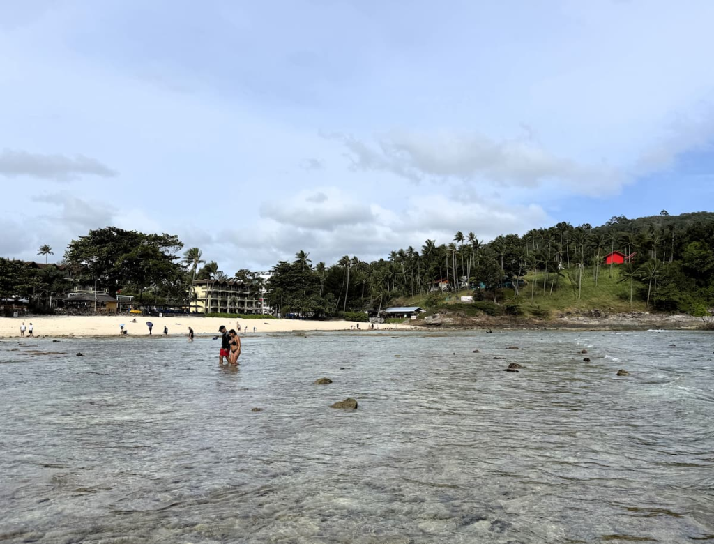 Visitors exploring the shallow rocky shoreline at Merlin Beach during lower tide
