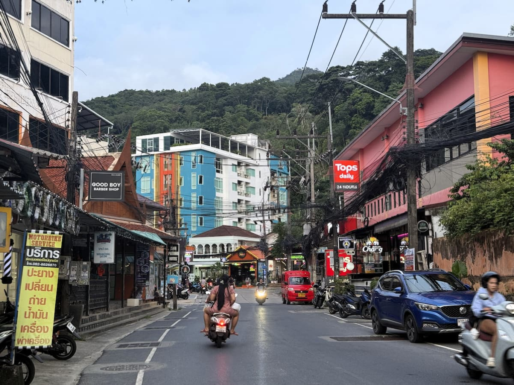 Nanai Road street scene in Patong with scooters, shops, overhead cables and hillside buildings