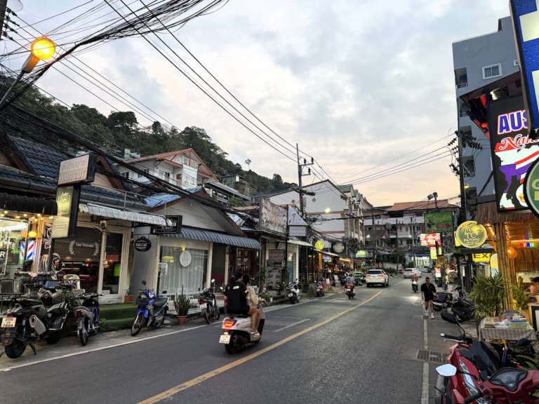 Nanai Road in Patong at dusk with shops, scooters, traffic and hillside buildings