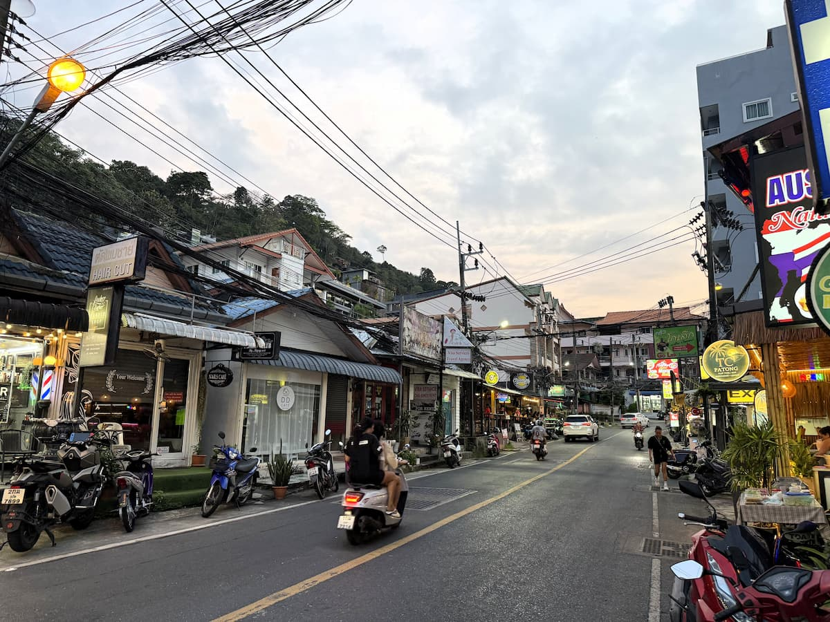 Nanai Road in Patong at dusk with shops, scooters, traffic and hillside buildings