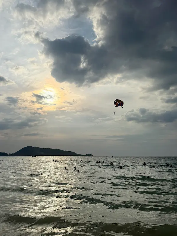 Parasailing above Patong Beach during the late afternoon, with swimmers enjoying the warm waters of Phuket's west coast.