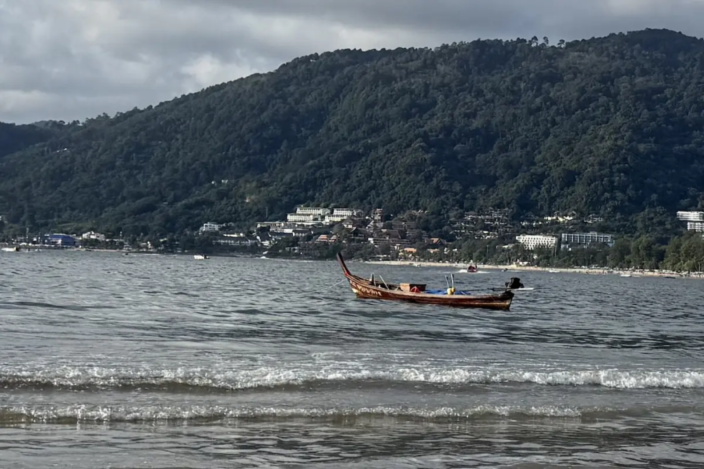 A traditional long-tail boat anchored off Patong Beach with Phuket's coastline featured in our Patong Travel Guide.