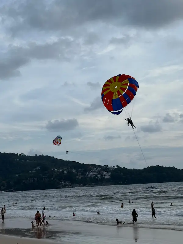 Visitors parasailing above Patong Beach while swimmers enjoy the water below on Phuket's west coast.