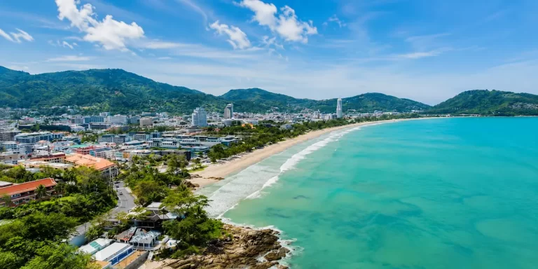 Elevated panoramic view of Patong Beach in Phuket showing the crescent-shaped bay, beachfront, resort town and surrounding forested hills.