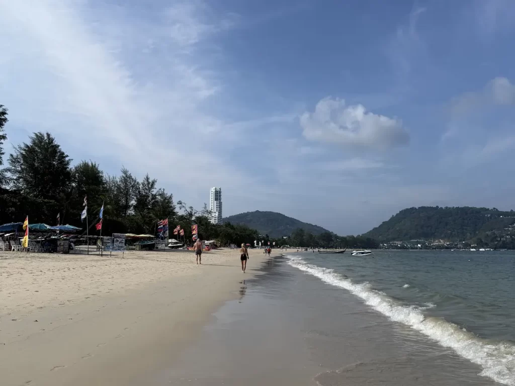 Patong Beach in Phuket, Thailand, with its long sandy shoreline, gentle waves and surrounding tropical hills.