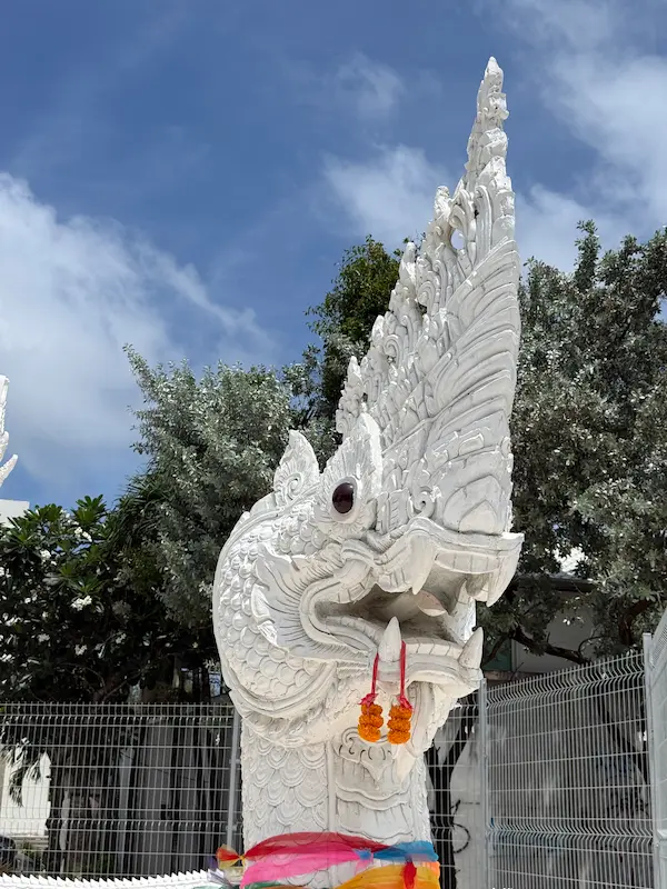 Close-up of the white Naga guardian statue at the entrance to the Patong Phra Phrom Shrine in Phuket, showing intricate traditional Thai carvings and marigold garlands.