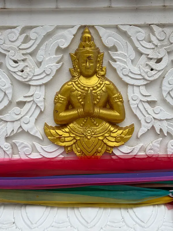 Golden relief of a devotee in the wai position decorating the base of the Patong Phra Phrom Shrine in Phuket.