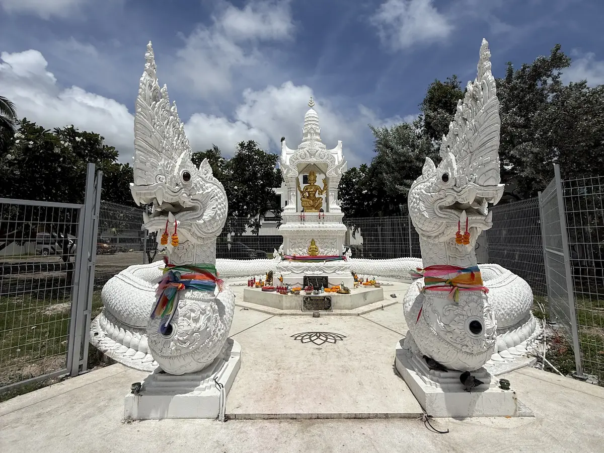 Phra Phrom Shrine near Dolphin Roundabout in Patong, framed by two white naga statues beneath a blue sky.