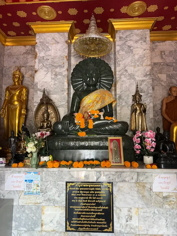 Principal Buddha image inside the sacred chedi at Wat Doi Thep Nimit in Phuket, surrounded by devotional offerings and revered Buddhist figures.