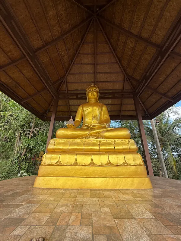 Large seated Buddha statue inside an open sala at Wat Doi Thep Nimit in Phuket near the entrance to the hillside monastery.
