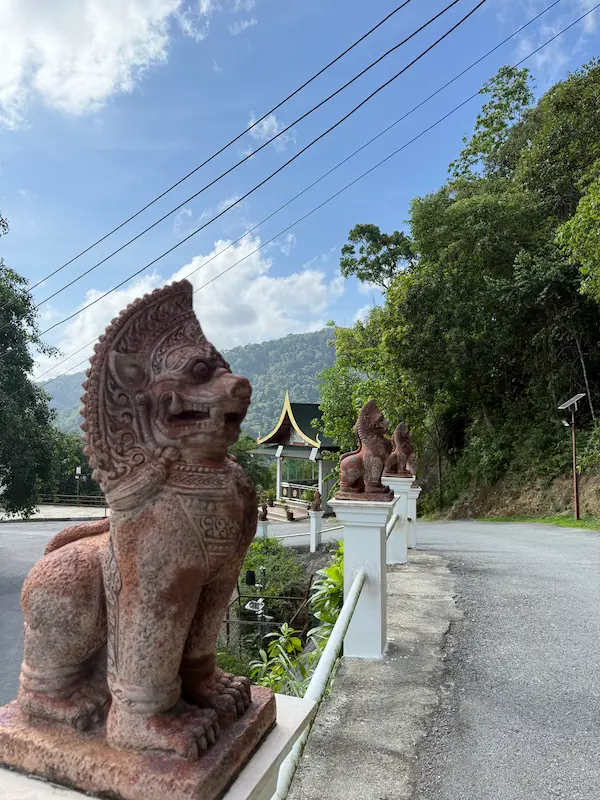Stone Singha guardian statues lining the entrance road at Wat Doi Thep Nimit in Phuket.