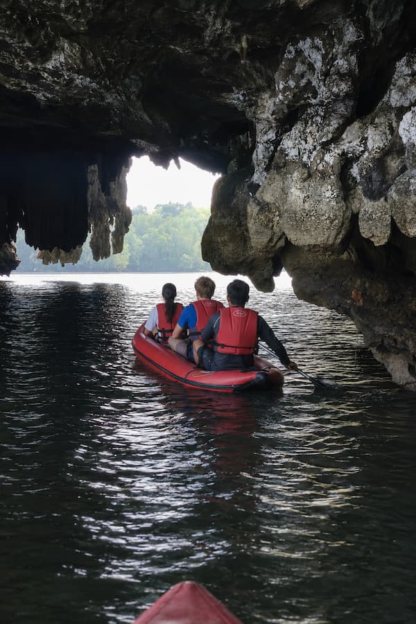Visitors in a guided canoe beneath a limestone sea cave in Phang Nga Bay, featured in our Phuket travel guide.