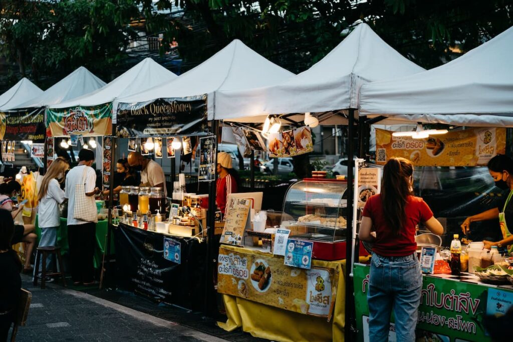 Food vendors serving customers at an outdoor street market in Bangkok, Thailand.