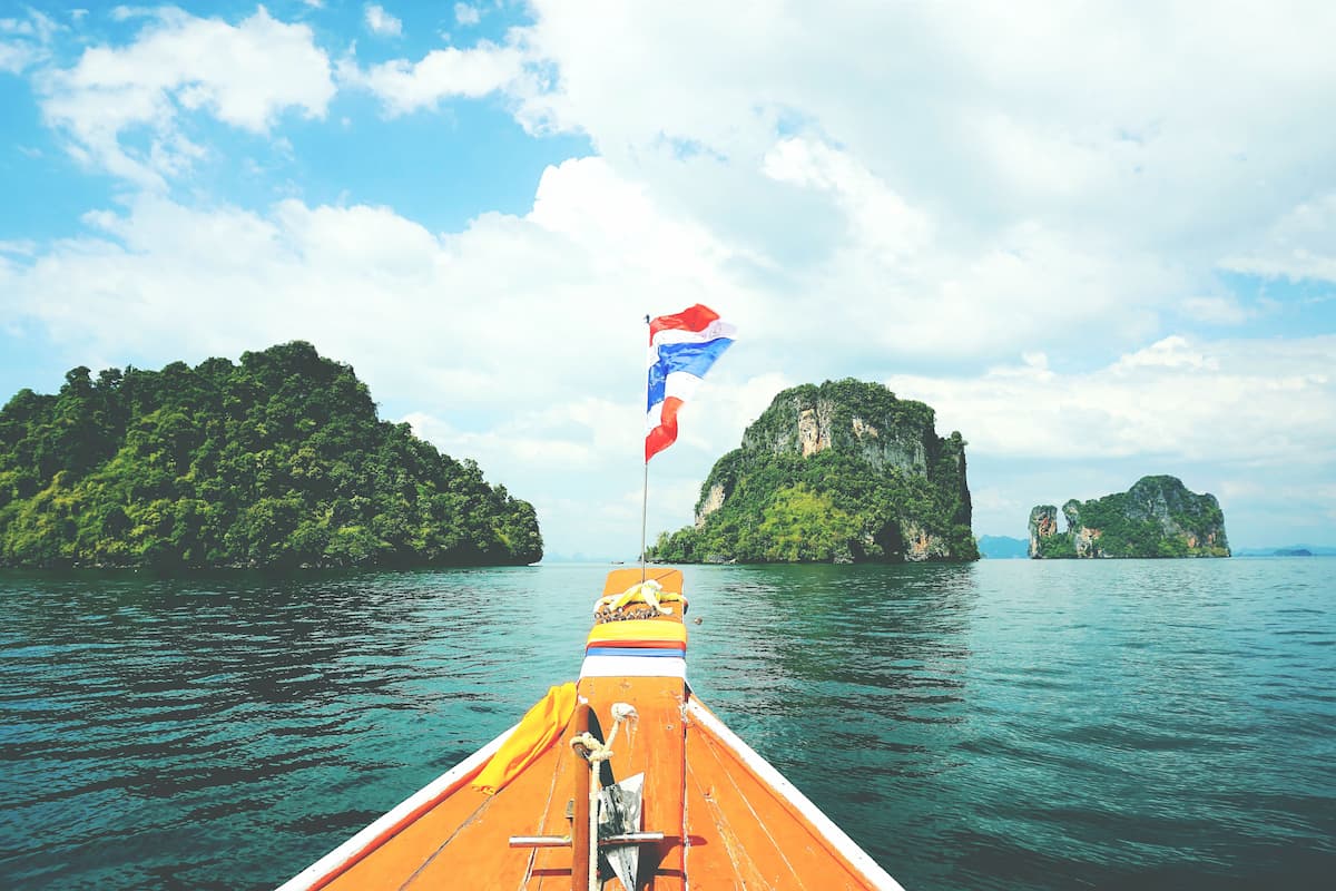 Longtail boat with a Thai flag travelling towards tropical islands in Southern Thailand for featured image in bext islands in southern thailand