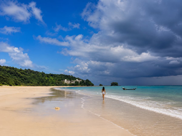 Best time to visit Southern Thailand with sunshine and tropical storm clouds over a quiet beach.
