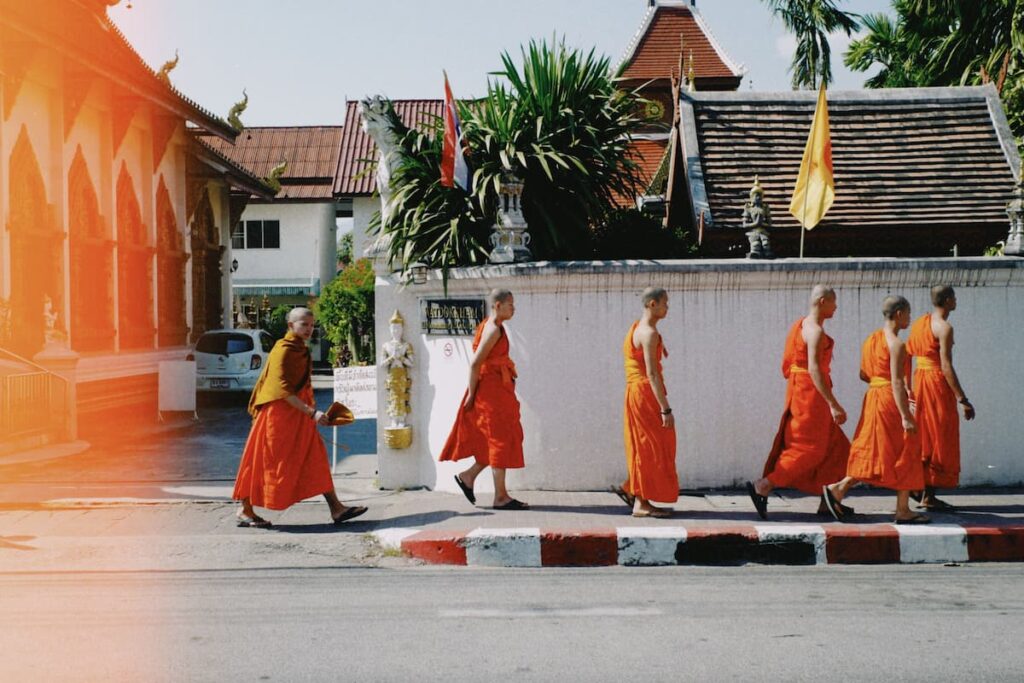 Buddhist monks walking beside a traditional temple in Chiang Mai, Thailand.