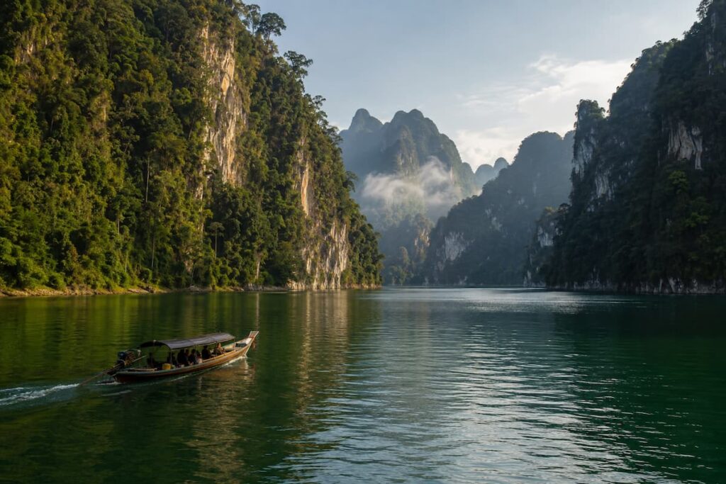 Longtail boat travelling across Cheow Lan Lake between rainforest-covered limestone cliffs