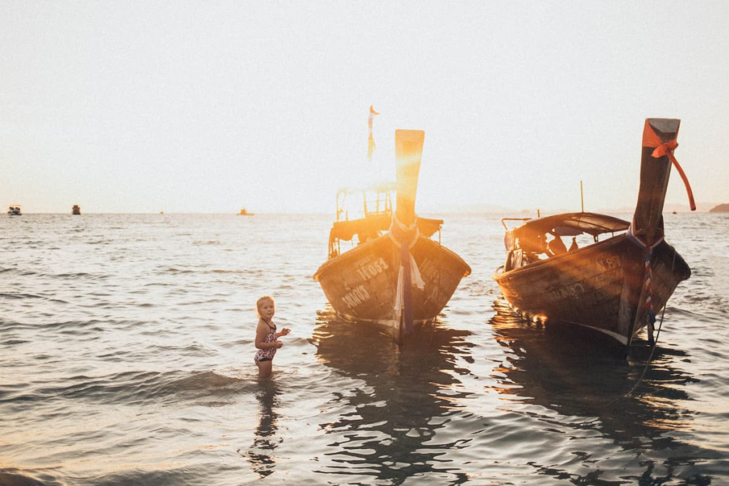 A child in shallow water beside longtail boats at Ao Nang, illustrating travel in Southern Thailand with children.
