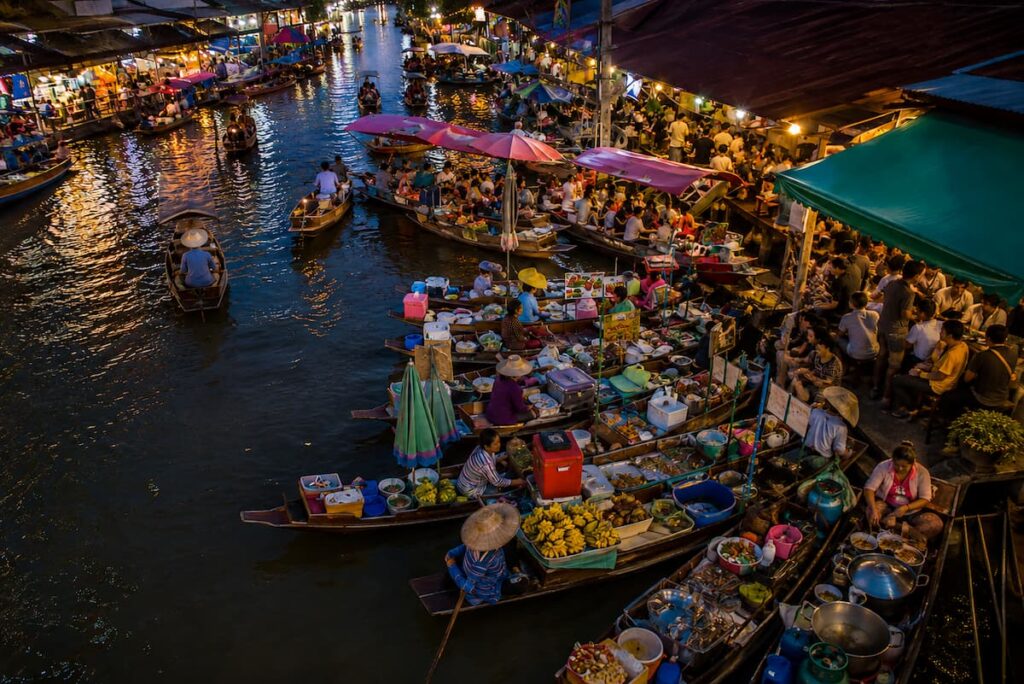 Floating markets in Thailand with food vendors in wooden boats along a busy canal in the evening