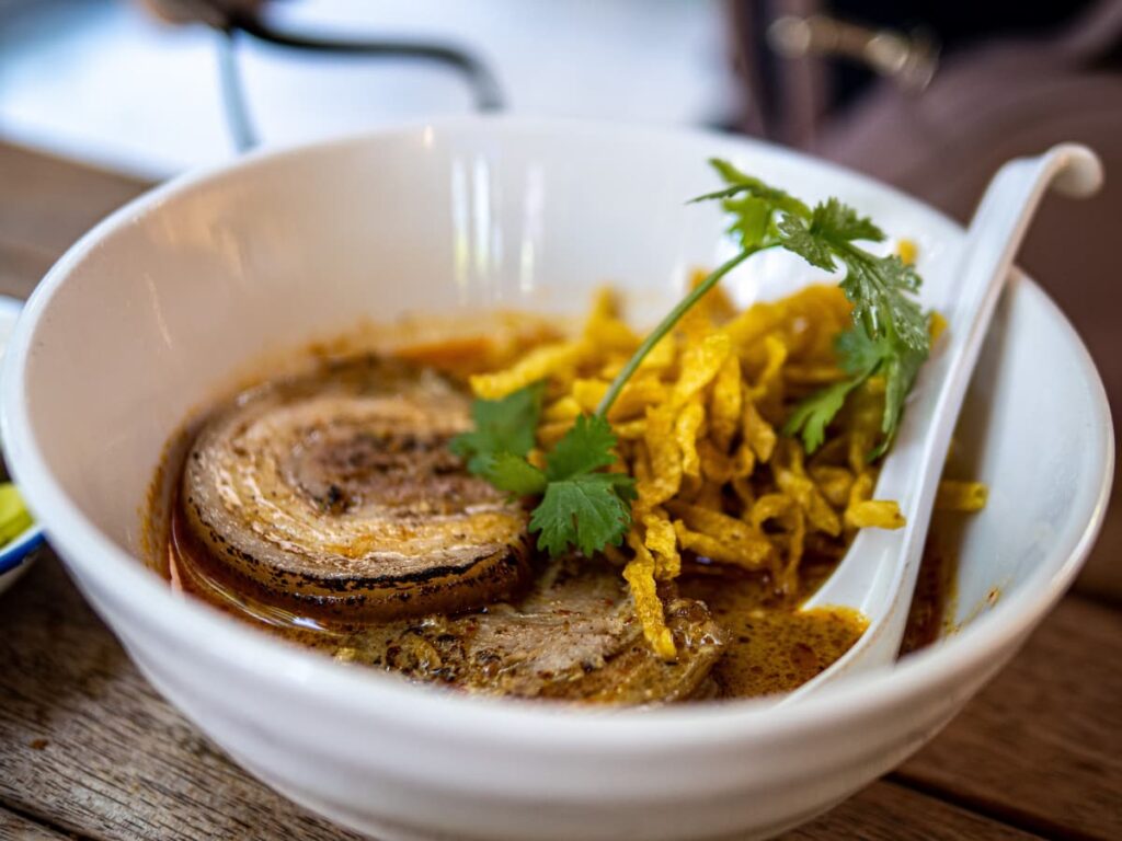 Bowl of khao soi with curry broth and crispy noodles in Chiang Mai, Thailand.