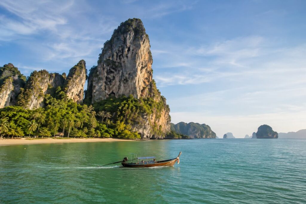 Traditional longtail boat passing limestone cliffs along the Krabi coastline in Southern Thailand