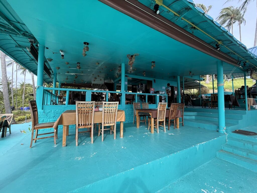 Open-air dining area inside Little Tiger Restaurant in Patong, with simple wooden tables and its distinctive turquoise interior.