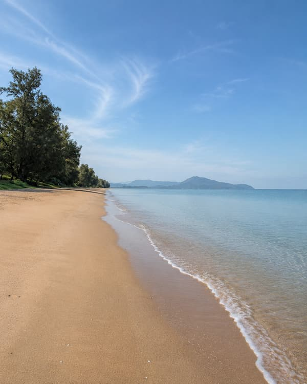 Tree-lined sands and gentle waves at Mai Khao Beach, featured in our Phuket travel guide.