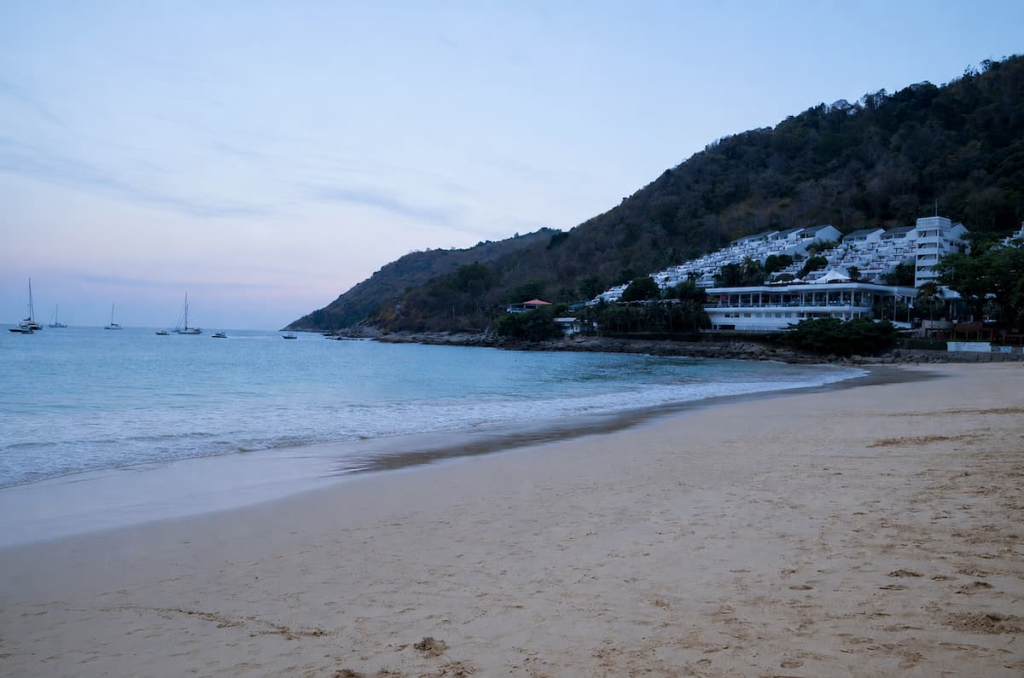 Nai Harn Beach in soft morning light, with yachts anchored beneath the surrounding green hills.