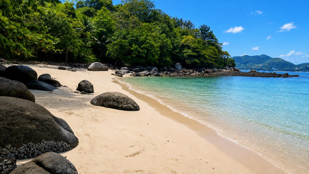 Quiet sandy cove at Paradise Beach near Patong, with clear water, granite boulders and a forested hillside on a sunny day.
