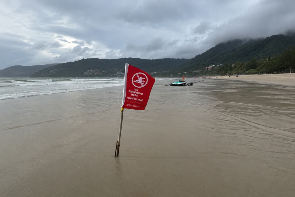 Red No Swimming Here warning flag on Patong Beach during rough, overcast sea conditions.