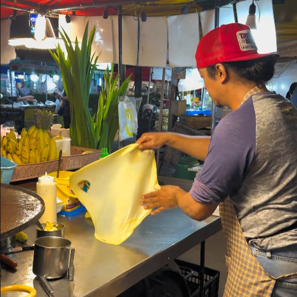 A Thai street food vendor stretching fresh roti dough by hand at a night market in Patong, Phuket, featured in our Patong Travel Guide.