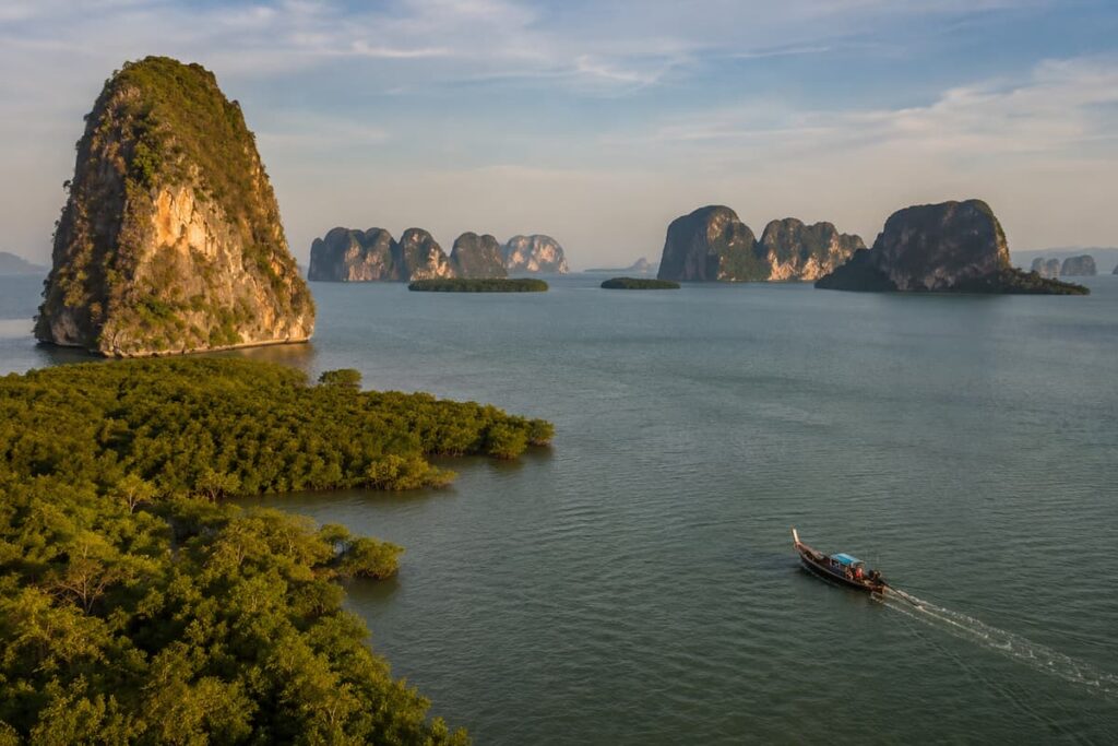 Longtail boat travelling through Phang Nga Bay among mangroves and limestone karsts