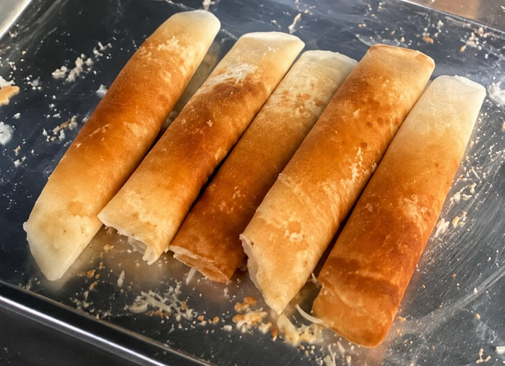 Rolled Phuket khanom a-pong coconut pancakes with crisp golden centres and pale edges.