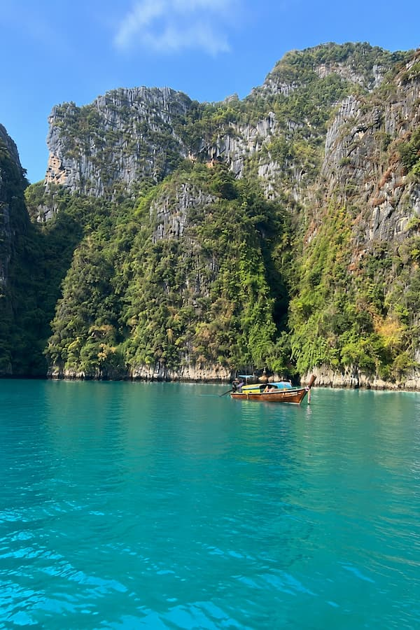 Long-tail boat beneath limestone cliffs in Pileh Lagoon’s turquoise waters, featured in our Phuket travel guide.