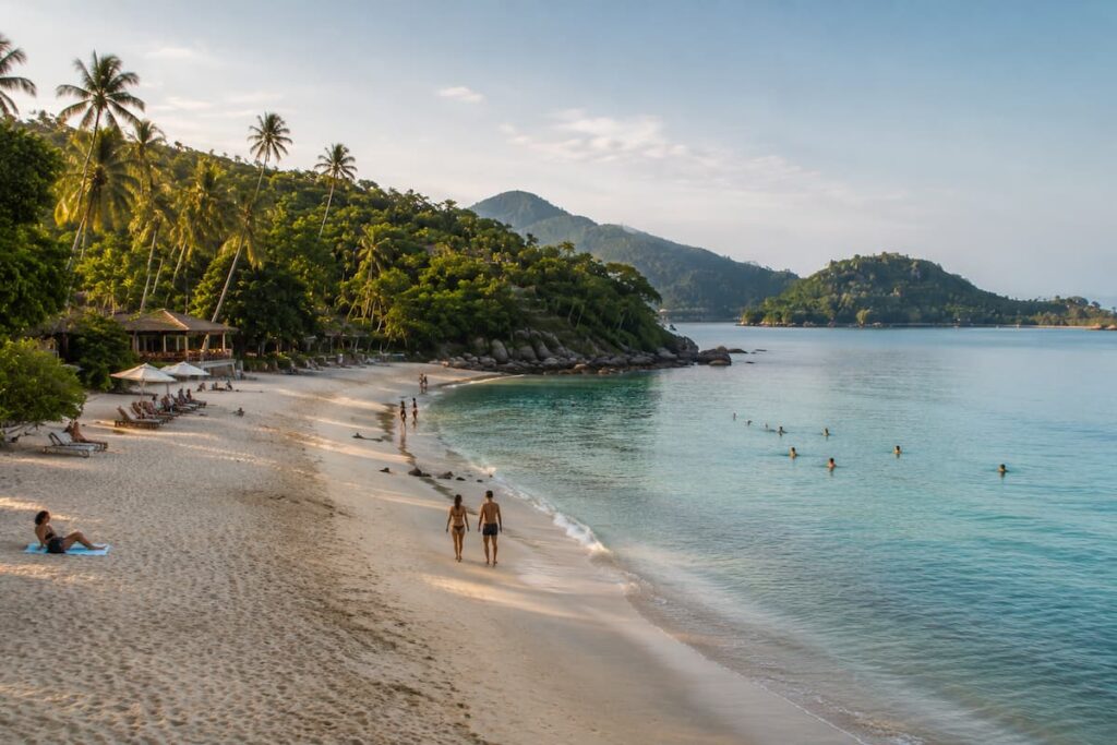 Visitors swimming and walking along a tropical resort beach in Southern Thailand
