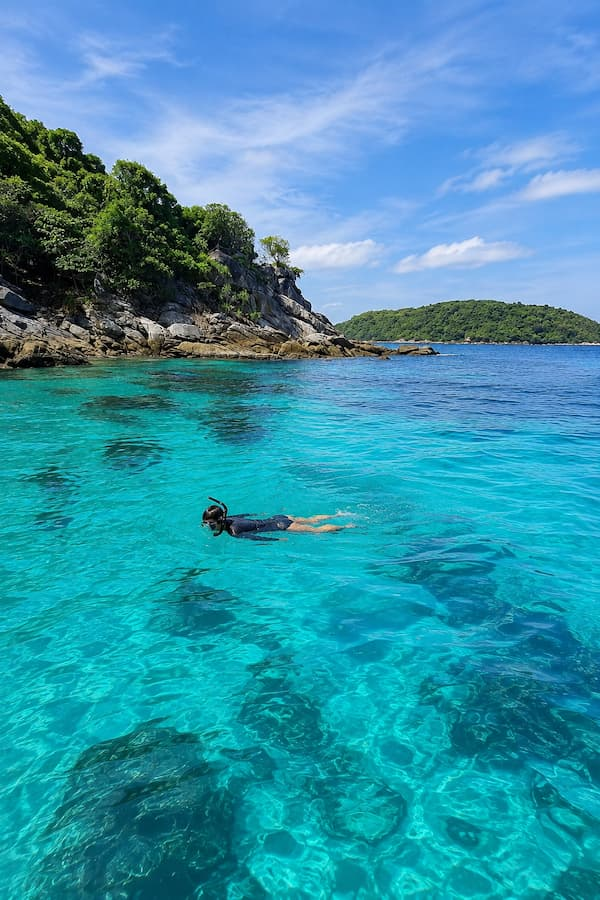Snorkeller in turquoise water beside Racha Yai’s rocky coastline, featured in our Phuket travel guide.