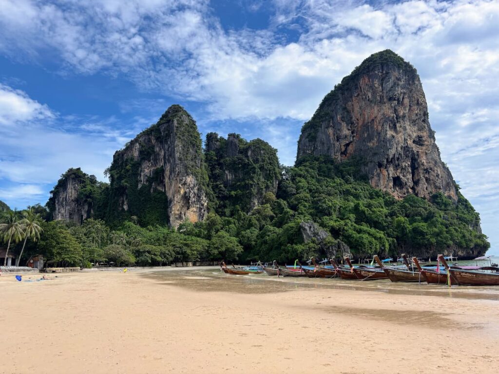 Longtail boats beneath towering limestone cliffs at Railay Beach in Krabi, Thailand