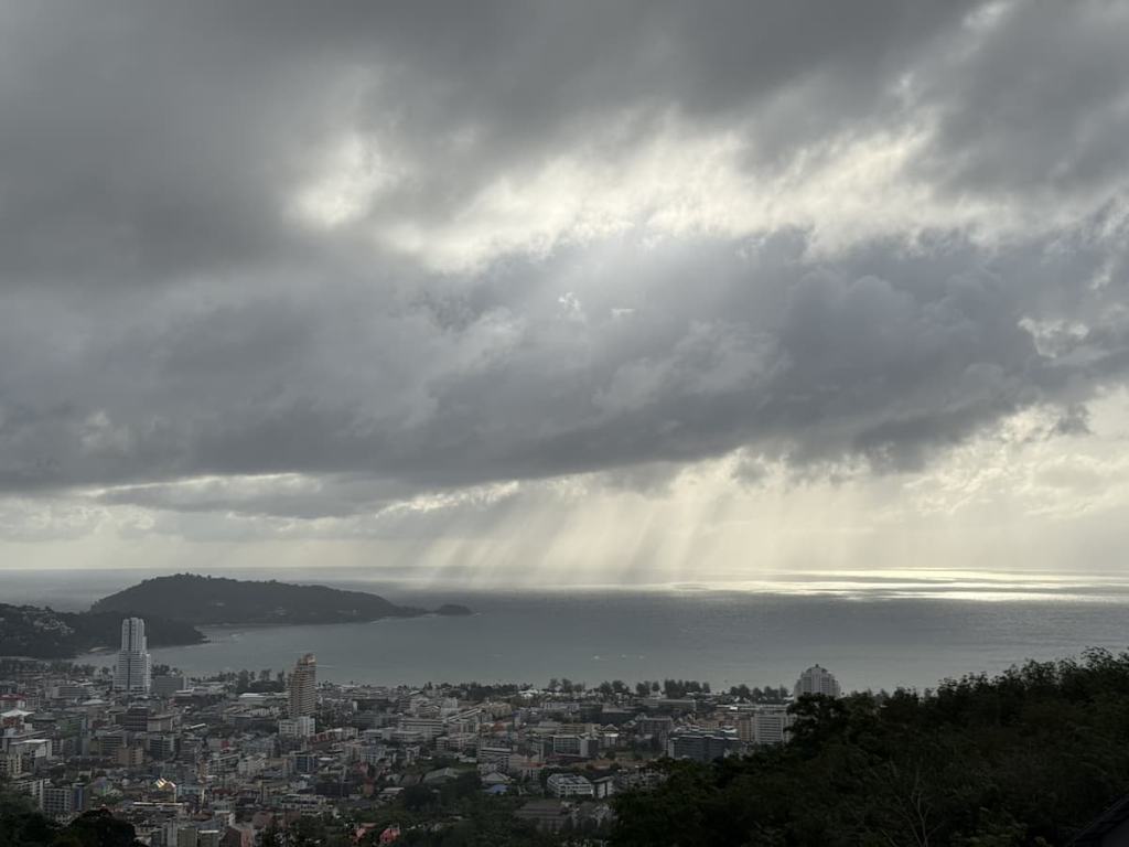 Localised rain showers moving across Patong Bay beneath dark tropical clouds, viewed from the hills above Patong.